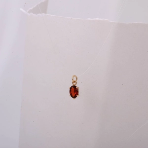 Detalle de un colgante ovalado de circón rojo con engaste de cuatro garras doradas