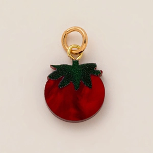 Détail d'un pendentif en forme de tomate rouge avec feuilles vertes et anneaux dorés