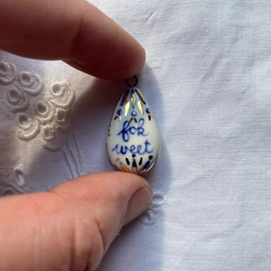 Primer plano de un colgante de cerámica blanca con diseño floral azul y el texto for sweet