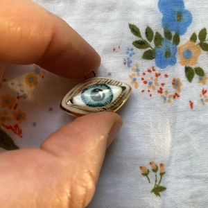 Primer plano del colgante de ojo en acero de titanio con iris azul y bordes dorados