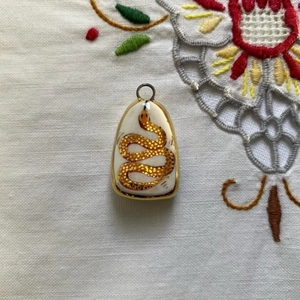 Vista detallada del colgante de gota con tótem de serpiente dorada en fondo porcelana