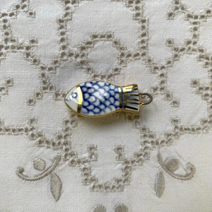 Colgante de pez de cerámica azul y blanca con bordes dorados sobre mantel de encaje
