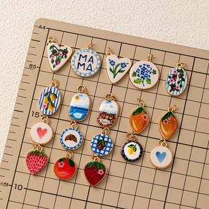 Bunte Emaille-Anhänger mit Blumen und Herzen auf einer Schneidematte für DIY