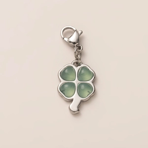 Detailed close-up of a silver four-leaf clover pendant with green heart-shaped resin stones