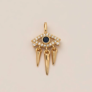 Pendentif œil grec plaqué or 18K avec pierre bleue et pampilles sur fond beige neutre