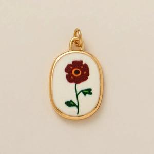 Détail macro du pendentif ovale doré avec illustration de fleur rouge rétro sur blanc