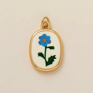 Détail d'un pendentif ovale doré avec fleur bleue imprimée sur émail blanc poli