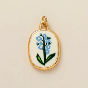Vue détaillée d'un pendentif ovale doré avec fleurs bleues sur base en céramique