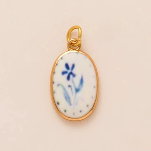 Detail van ovale titaanstalen hanger met blauwe bloemmotieven en gouden frame