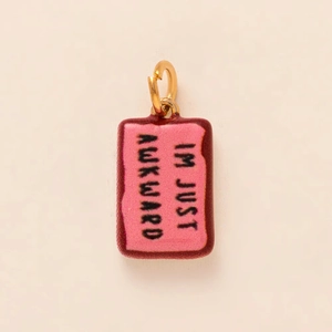 Detail of pink and red enamel rectangular charm with IM JUST AWKWARD text in gold plating