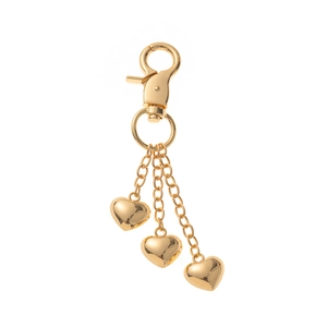 Macro shot of three golden heart charms on chains with polished mirror finish and lobster clasp