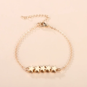 Minimalistische gouden sterrenarmband met vijf bedeltjes op een roze achtergrond