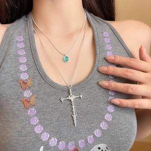 Close-up of gothic thorn cross and light blue gemstone layered necklaces on a model
