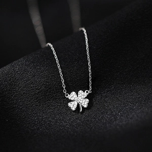 Silver four-leaf clover pendant necklace with sparkling pavé crystals on a black fabric background