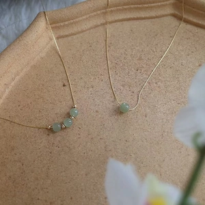 Elegant gold chain necklace with green jade beads on a textured tray with flowers