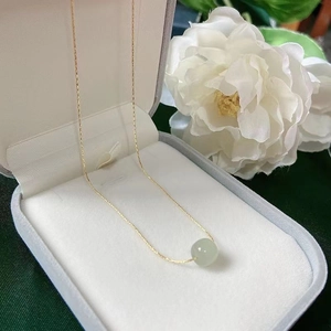Close-up of gold chain necklace with a light green jade bead in a grey jewelry box