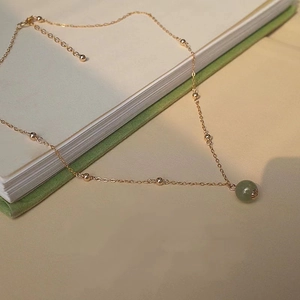 Elegant gold necklace with green Hetian jade pendant over a vintage book background