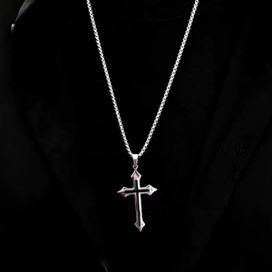 Detail shot of a silver gothic cross pendant with black enamel inlay on a curb chain
