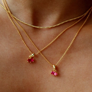 Close-up of triple layered gold necklaces with marquise-cut pink gemstone pendants