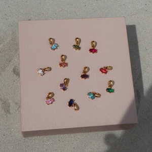 Marquise-cut birthstone pendants with gold plating set on a pink jewelry box in sunlight