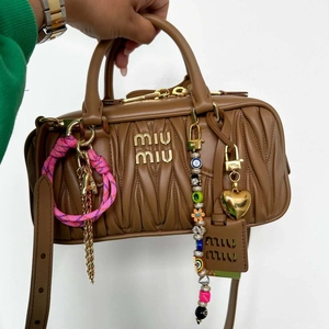 Brown quilted leather bag with alphabet charms and gold heart pendant on white background