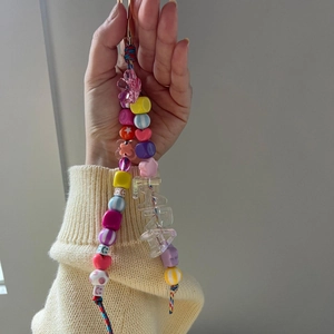 Colorful beaded phone lanyard with LARA alphabet beads and various charms held by hand