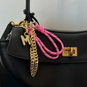 Close-up of golden letter M charm with pink woven rope on a black leather handbag