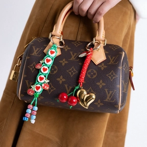 Detail of colorful woven cherry and heart charms on a classic patterned luxury handbag