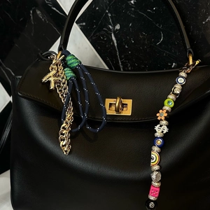Detail of luxury black leather handbag featuring golden horse charm and beaded keychains