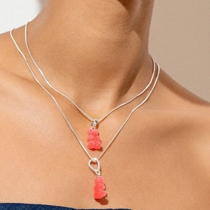 Close-up of a model wearing layered silver necklaces with red gummy bear pendants