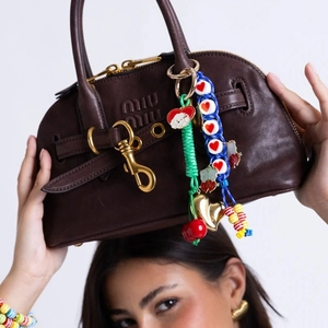 Detail of colorful woven rope bag charms with cherry and heart pendants on leather bag