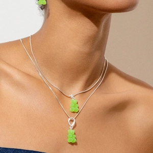 Detail of layered silver necklaces and earrings with green gummy bear resin charms
