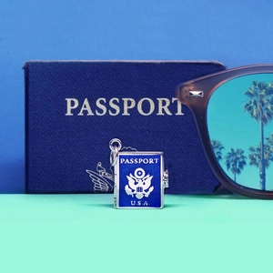 Detailed blue enamel passport charm on travel background with sunglasses and passport