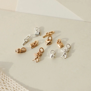 Vista macro di vari mini ciondoli in oro e argento, inclusi lucchetto, chiave e cuori
