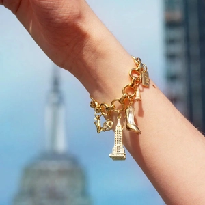 Gold charm bracelet with NYC taxi and Empire State Building pendants over a city skyline