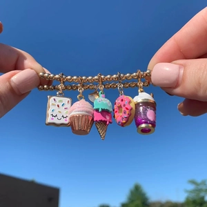 Close-up of golden beaded bracelet with enamel dessert charms against a blue sky