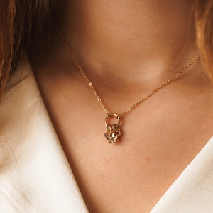 Dettaglio di una collana dorata con ciondolo a fiore, chiave e gemma viola indossata