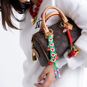 Handmade woven bag charms with cherry and heart pendants on luxury monogram bag