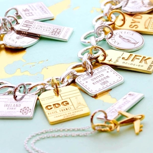 Detailed macro view of 18K gold-plated travel pendants with city airport codes on a map