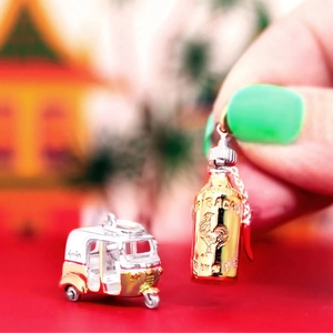 Macro detail of Sriracha sauce bottle and Tuk Tuk car charms with metallic finish