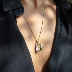 Detail von Vintage-Goldmünzen- und weißen Emaille-Federanhängern an einer Goldkette