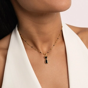 Primer plano de cadena dorada con cuentas y colgante de gato negro en el cuello de modelo
