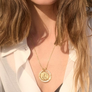 Detail einer goldenen Münzhalskette mit Heiligenrelief und funkelnden Kristallen an einem Model