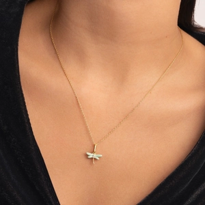Detalle de un collar de libélula dorada con alas de esmalte verde sobre fondo de terciopelo negro