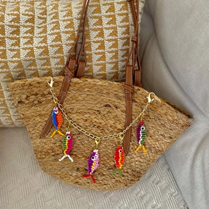 Detail of colorful beaded fish charms on a woven tote bag with a golden metal chain