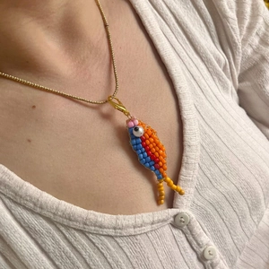 Colorful beaded fish pendant necklace with gold chain worn on white ribbed shirt