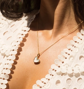 Detail van een 18K vergulde hartvormige hanger met witte schelp op de hals van model