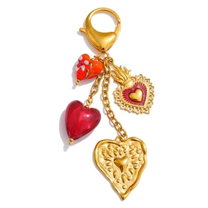 Detail of golden keychain with red glass hearts and floral charms on white background