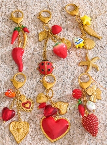 Detail of vibrant gold lobster clasps with red strawberry, chili, and heart pendants on sand