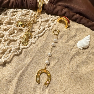 Golden seahorse pendant with pearls and shell charm on beach sand with white fishnet